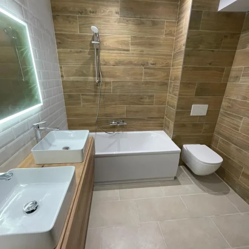 Salle de bain rénovée avec baignoire et carreaux métro blanc et effet bois.